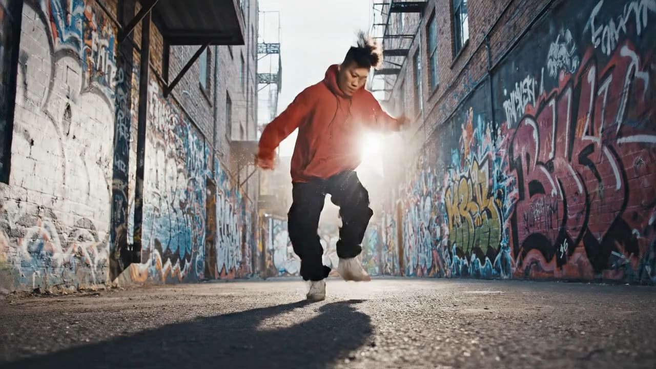 Dynamic street dancer performing fluid breakdance moves in an urban alley with graffiti walls, dramatic side lighting, slow motion spin, energetic movement